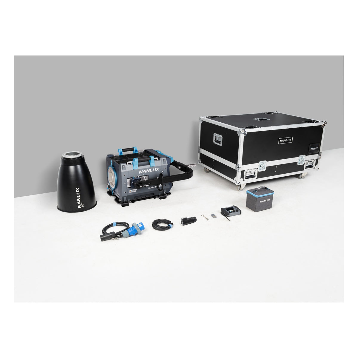 Complete NANLUX Evoke 5000B-KIT displayed on white surface showing the gray light head with blue accents, conical reflector, flight case with latches, remote controller, cables, and small accessories arranged left to right.