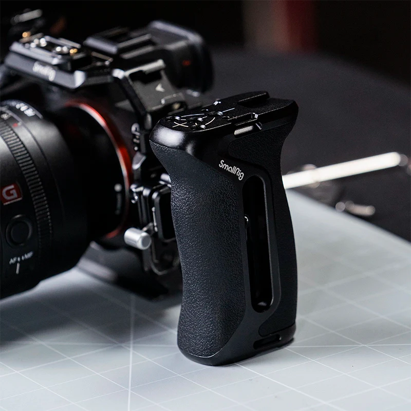 Close-up of a SmallRig side handle mounted on a cinema camera cage, showing textured grip and aluminum build on a grey tabletop.