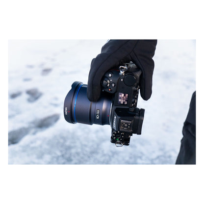 Laowa 10mm mounted on Nikon Z mirrorless camera held in gloved hands over snowy landscape.