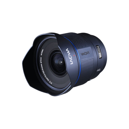 Laowa 12mm f/2.8 captured at a dynamic 45-degree angle showing the lens profile, hood geometry, and rear mount assembly against white background with visible interior glass elements.