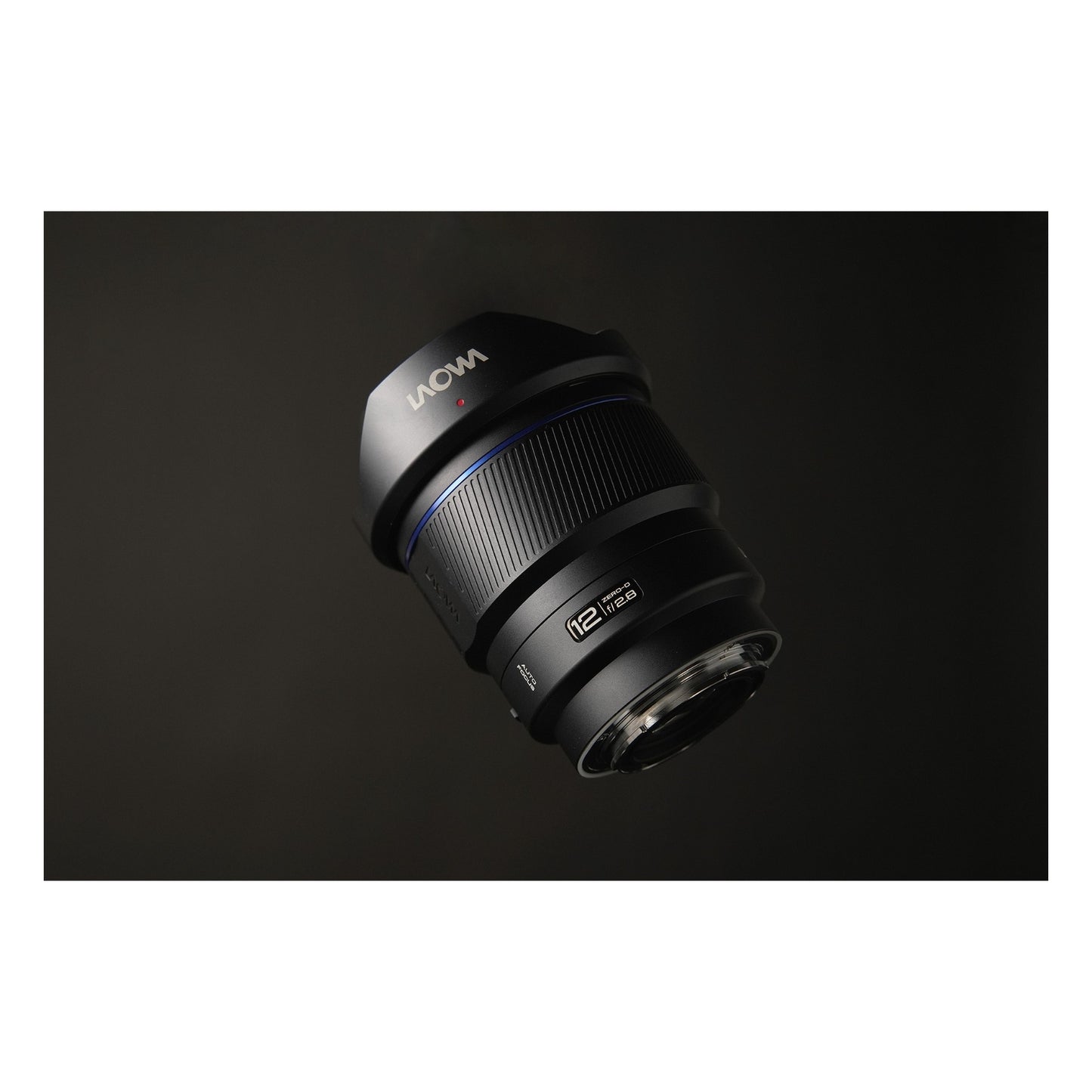 Laowa 12mm f/2.8 photographed from above against a dark gradient background, hovering position emphasizing the barrel geometry and hood form with even, subtle side-lighting.