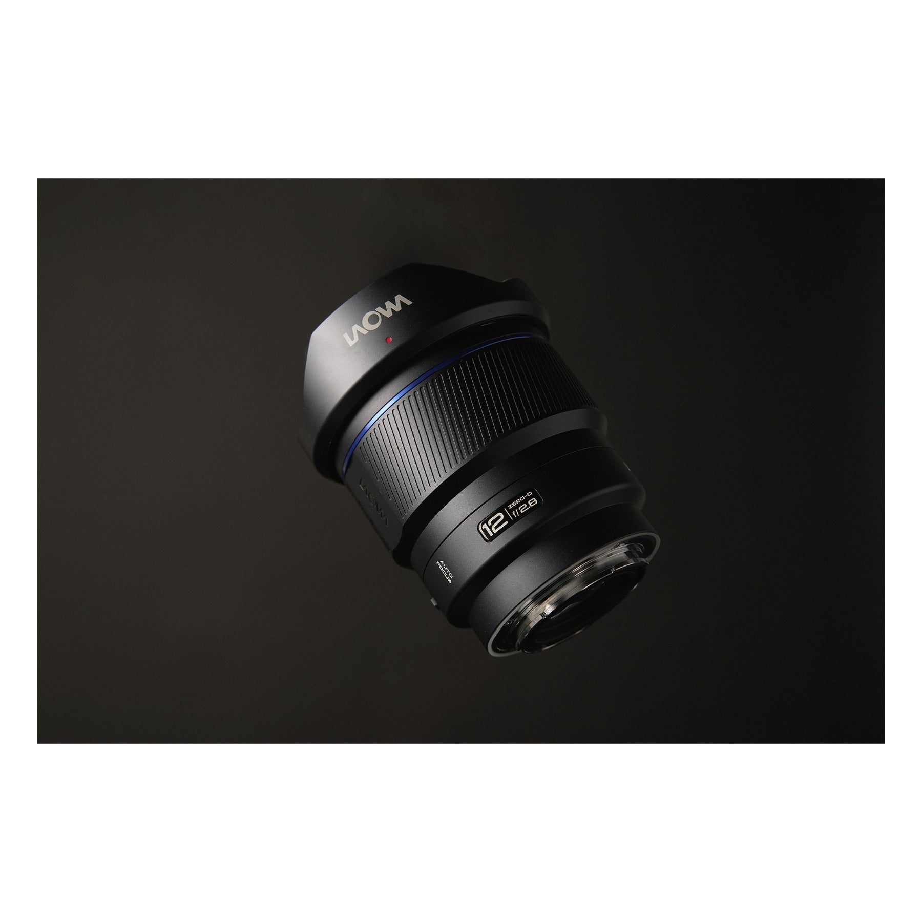 Laowa 12mm f/2.8 photographed from above against a dark gradient background, hovering position emphasizing the barrel geometry and hood form with even, subtle side-lighting.