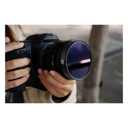 Laowa 12mm T2.9 Lite Zero-D lens mounted on cinema camera in hands outdoors, showing lens in field use with blurred architectural background.